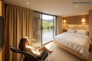 Moderne hut op de MS Veloria met tweepersoonsbed, groot raam met uitzicht op rivier en wijngaarden, vrouw ontspant in stoel. Warme houttinten.