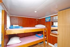 Compacte scheepshut op MS Kazimir met houten stapelbedden, witte kussens, blauwe handdoeken en houten wandbekleding. Klein raam en kast zichtbaar.