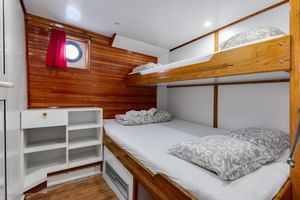 Compacte scheepshut op MS Mirabela met houten stapelbedden, wit beddengoed, patrijspoort met rood gordijn en witte opbergkast.