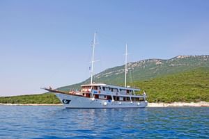 Witte motoryacht MS Amore met twee masten voor anker in blauw water nabij een groen Kroatisch eiland met rotsachtige heuvels.
