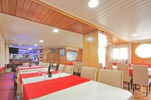 Interieur van Kazimir boot bar met eetruimte, witte tafels, rode tafelkleden, beige stoelen, houten lambrisering en ronde ramen.
