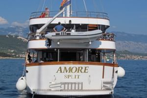 Achterzijde van wit zeilschip MS Amore uit Split voor anker in blauw water met Kroatische bergen en kust op de achtergrond.