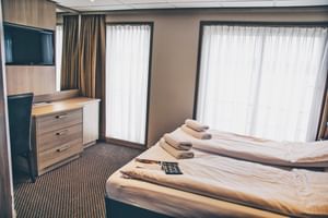 Moderne scheepshut met tweepersoonsbed, wit beddengoed, handdoeken, TV, houten meubels en grote ramen met witte gordijnen op MS DE WILLEMSTAD.