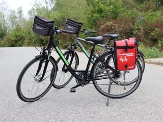 Twee zwarte toerfietsen met 24 versnellingen geparkeerd op een weg, uitgerust met zwarte stuurstassen en een rode achtertas.