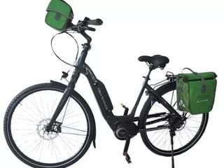 Zwarte e-bike met lage instap, schijfremmen en groene fietstassen gemonteerd op stuur en achterdrager op witte achtergrond.