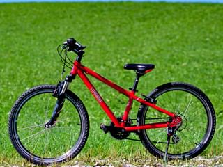 Rode Eurobike kinderfiets met zwarte onderdelen geplaatst op groen grasveld met blauwe lucht op de achtergrond.