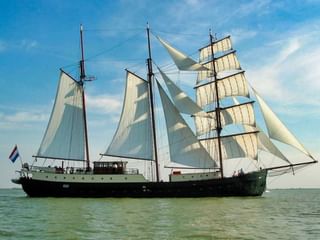 Driemast zeilschip Simmer Fan Fryslân met witte zeilen op kalm water onder blauwe hemel met wolken.
