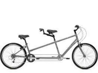 Zilveren tandemfiets met twee zadels en sturen, ontworpen voor twee fietsers om samen te fietsen, in zijaanzicht op witte achtergrond.
