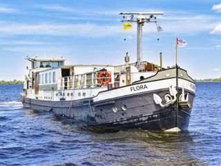 MS Flora, een wit en zwart passagiersschip met blauwe ramen, varend op kalm water onder een blauwe lucht met witte wolken.