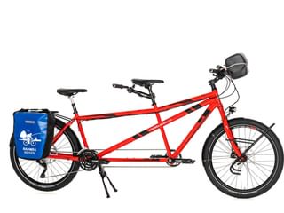 Rode tandemfiets met twee zitplaatsen, zwarte zadels, blauwe achtertassen, grijze stuurtas en standaard op witte achtergrond.