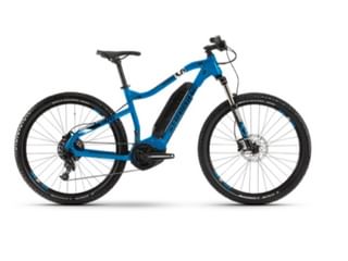 Blauwe elektrische mountainbike met zwarte motor, voorvering, schijfremmen en noppen banden op witte achtergrond.