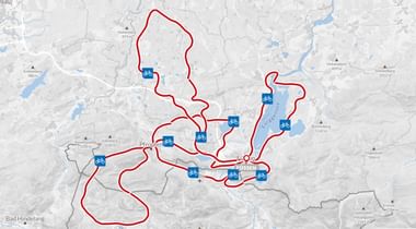 Kaart met meerdere rode fietsroutes die uitwaaieren vanuit een centraal punt in de Allgäu-regio. Blauwe fietspictogrammen markeren belangrijke locaties.