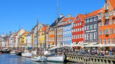 Historische kleurrijke herenhuizen langs het Nyhavn-kanaal in Kopenhagen met traditionele zeilboten aangemeerd onder blauwe hemel.