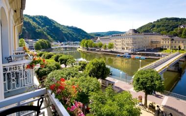 Balkonuitzicht van Häckers Grand Hotel Bad Ems op de Lahn rivier, historische gebouwen, groene heuvels en kleurrijke bloemen.