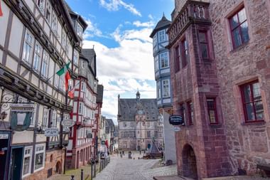 Kinderkopjes marktplein in Marburg omringd door vakwerkhuizen en stenen gebouwen. Gotisch stadhuis domineert de achtergrond.