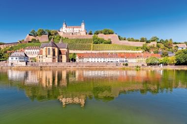 Festung Marienberg fort op een heuvel met wijngaarden in Würzburg, weerspiegeld in de Main. Kleurrijke gebouwen langs de waterkant.