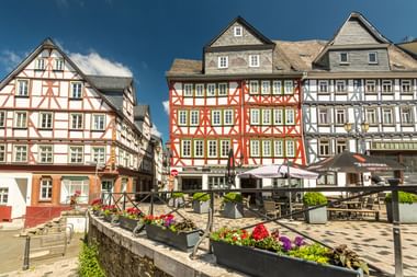 Historisch Kornmarkt plein in Wetzlar met kleurrijke vakwerkhuizen, buitenterrassen en bloembakken onder blauwe hemel.