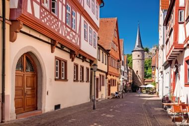 Smalle geplaveide straat in Karlstadt met traditionele vakwerkhuizen. Een middeleeuwse stenen toren met spitse torenspits rijst op de achtergrond.