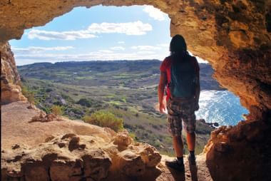 Calypso grot uitzicht in Gozo, Malta Persoon met rugzak in Calypso grot opening met uitzicht op Ramla Bay en platteland in Gozo, Malta met blauwe zee en bewolkte lucht.