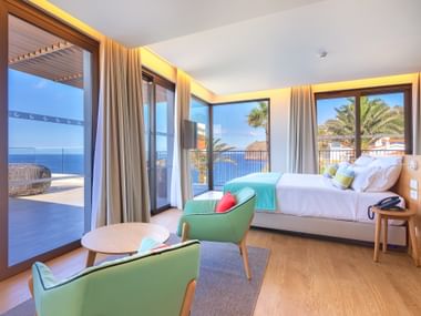 Moderne hotelkamer met oceaanzicht in Hotel Galomar met wit bed, groene stoelen, houten vloer en grote ramen naar terras.