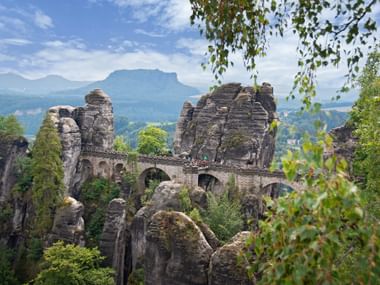 De historische Bastei Brug overspant hoge zandstenen rotsformaties in Saksisch Zwitserland, omgeven door groen bos.