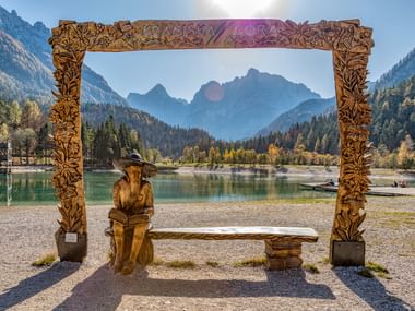 Sierlijke houten lijst met gesneden decoraties en zittende figuur, uitkijkend over alpenmeer en bergen in Kranjska Gora, Slovenië.