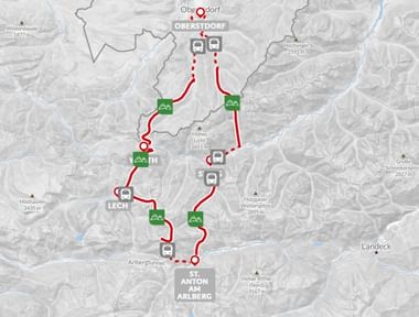 Wandelroutekaart met rode paden tussen Oberstdorf, Lech en Anton am Arlberg met groene accommodatiemarkeringen en bushaltes in de Alpen.