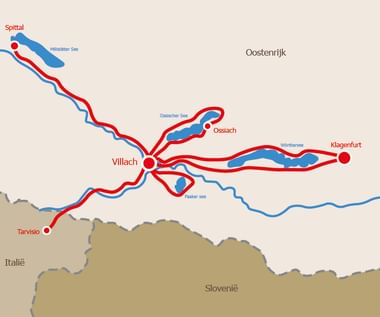 Kaart met fietsroutes in rode en blauwe lijnen die Villach verbinden met Spittal, Ossiach, Klagenfurt en Tarvisio in Oostenrijk, Italië en Slovenië.