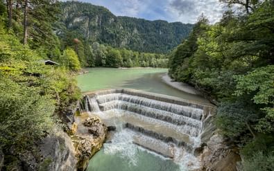 Lechfall stuw met getrapte betonstructuur die trapsgewijze watervallen creëert. Groene rivier stroomt door bebost dal met bergen.
