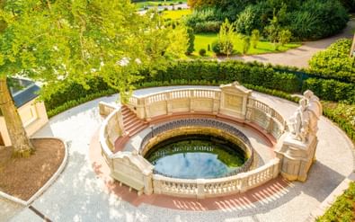Luchtfoto van de Donaubron, een ronde fontein met sierlijke balustrades en beelden, omringd door verzorgde tuinen in Donaueschingen.