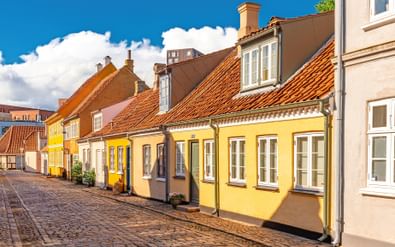 Rij traditionele Deense huizen met oranje pannendaken en gele gevels langs een kasseienstraat in Odense, Funen.