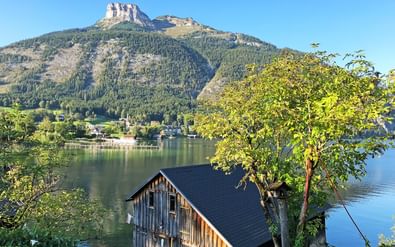Houten boothuis aan het Altaussee meer met beboste berg en rotsachtige top onder heldere blauwe hemel in Salzkammergut, Oostenrijk.