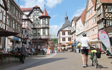 Historisch stadsplein in Lohr Geplaveide plein in de oude stad van Lohr met traditionele vakwerkhuizen, een kerktoren en een fietser met zijn fiets.