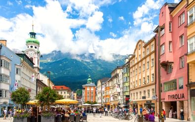 Voetgangerszone in Innsbruck met kleurrijke historische gebouwen, terrasjes en de Stadtturm klokkentoren. Alpenbergen zichtbaar op achtergrond.