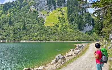Vrouw met rugzak en kind op oeverpad bij Spitzingsee. Groen meer omringd door beboste bergen en rotskloven in Beieren.