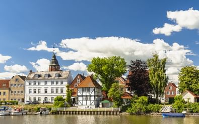 Waterkant van Glückstadt met historische gebouwen, waaronder een wit gebouw met toren en vakwerkhuis aan het water.