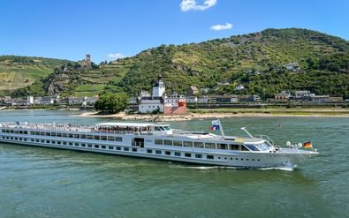Wit riviercruiseschip MS Arkona varend op de Rijn met kasteel Pfalzgrafenstein op een klein eiland en terrasvormige wijngaarden.