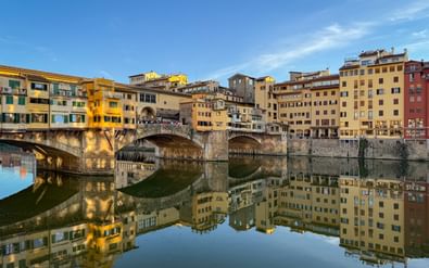 Ponte Vecchio brug met middeleeuwse gebouwen over de Arno in Florence. Perfecte spiegeling in kalm water onder blauwe lucht.