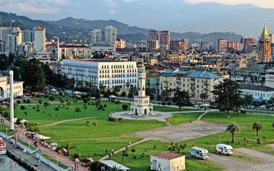 Luchtfoto van Batumi, Georgië met moderne gebouwen, groen park met klokkentoren, waterkant en bergen op de achtergrond bij zonsondergang.