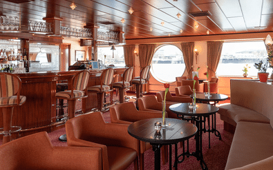 Interieur van MS Switzerland salon met houten bar, beige fauteuils, ronde tafels en ronde ramen met gordijnen met uitzicht op het water.