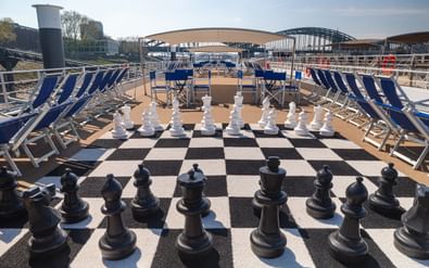 Zonnedek van MS Lisabelle met reuzenschaakspel op schaakbord, blauwe ligstoelen en rivierbruggen op de achtergrond.