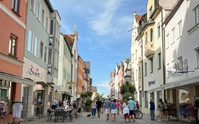 Geplaveide voetgangersstraat in Füssens centrum met kleurrijke historische gebouwen, winkels en wandelaars. Blauwe lucht met witte wolken.