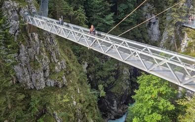 Witte metalen hangbrug over de Geisterklamm-kloof bij de Zugspitze. Een wandelaar steekt de brug over boven rotskloven en turquoise beek.
