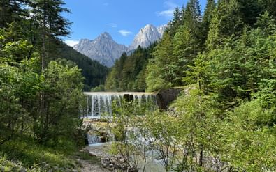 Waterval met meerdere niveaus in Kranjska Gora omgeven door dicht groen bos met dramatische kalkstenen pieken van de Julische Alpen.