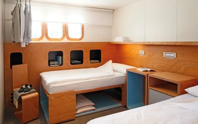 Compacte scheepshut met twee bedden, houten lambrisering, opbergnissen en raam. Wit beddengoed en moderne inrichting zorgen voor een gezellige ruimte.