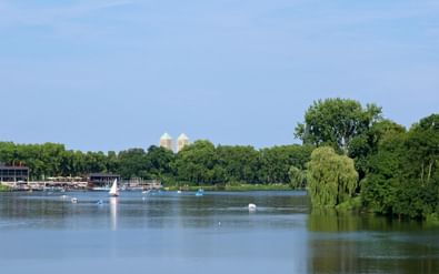 Panoramisch uitzicht op het Aasee meer in Münster met zeilboten op kalm water, omgeven door groene bomen en historische kerktorens op de achtergrond.