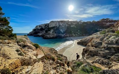 Schilderachtige Calo des Marmols baai op Mallorca met wit zandstrand, turquoise water, kalkstenen kliffen en een persoon op de kust.