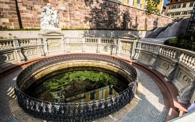 Rond stenen bassin met sierlijke ijzeren balustrade van de Donaubron in Donaueschingen, omgeven door barokke balustrade en sculptuur.