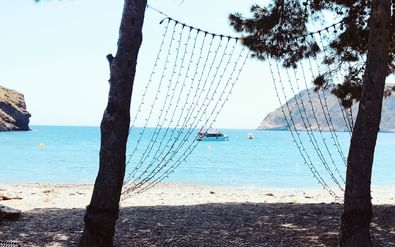 Uitzicht door hangmatkoorden naar turquoise Middellandse Zee bij Costa Brava strand met boten voor anker in de baai en rotsige kliffen.