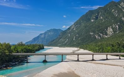 Brug over de turquoise Tagliamento bij Venzone met witte grindbanken en groene bergen op de achtergrond onder blauwe lucht.